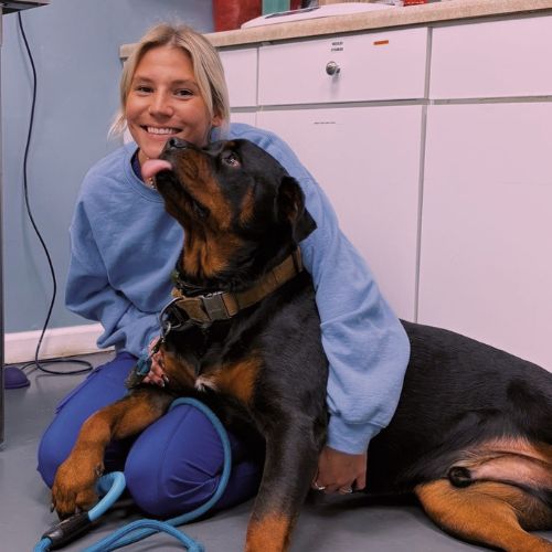 A woman sitting on the floor, smiling, with a dog